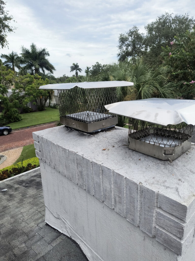 Two metal chimney caps installed on a white-painted brick chimney on a roof by A Sweep Across the Bay in Parrish, FL.