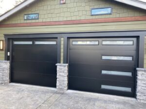 Two modern black garage doors with horizontal windows installed on a residential home by Independent Garage Doors LLC in Tacoma, WA.