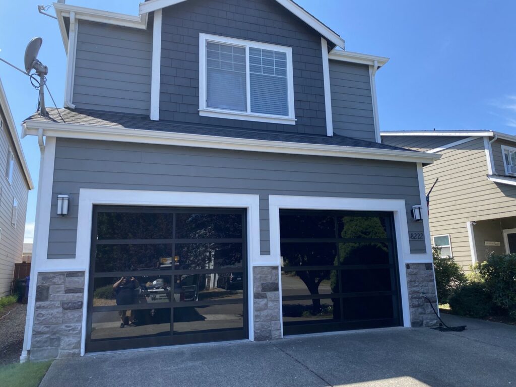 Two modern black glass garage doors installed on a residential home by Independent Garage Doors LLC in Tacoma, WA.