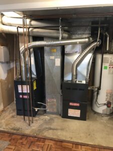 Two new Goodman furnaces and a water heater with ductwork installed in a basement utility area by EPIC Heating and Air in Loveland, CO