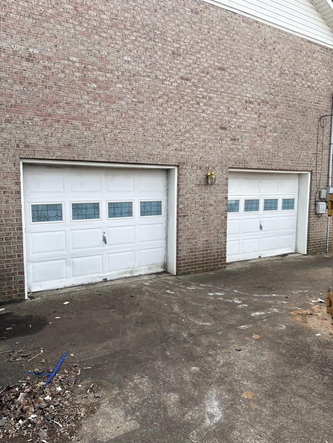 Two older white garage doors with decorative windows on a brick building, serviced by J&S Garage Door Services in Franklin, TN.