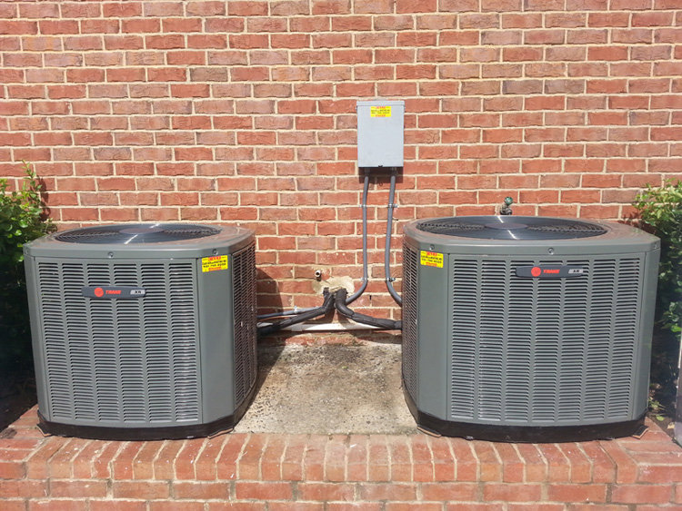 Two outdoor AC condenser units installed next to a brick building by C&K Air and Heating, Inc. in Olive Branch, MS.