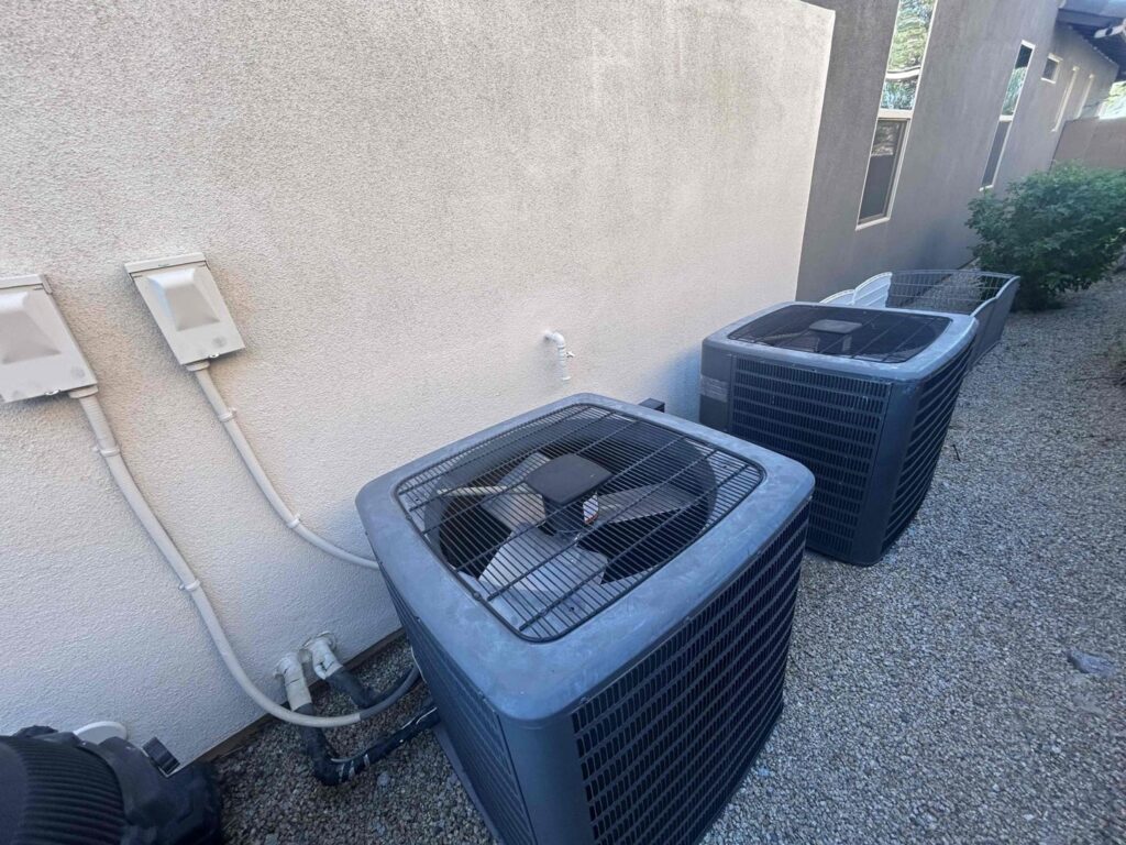 Two outdoor AC condenser units installed next to a residential building by One Hour Heating & Air Conditioning of West Valley in Phoenix, AZ