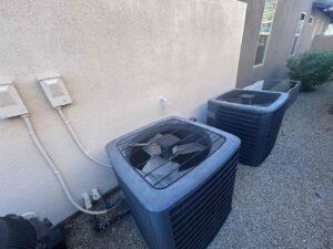 Two outdoor AC condenser units installed next to a residential building by One Hour Heating & Air Conditioning of West Valley in Phoenix, AZ
