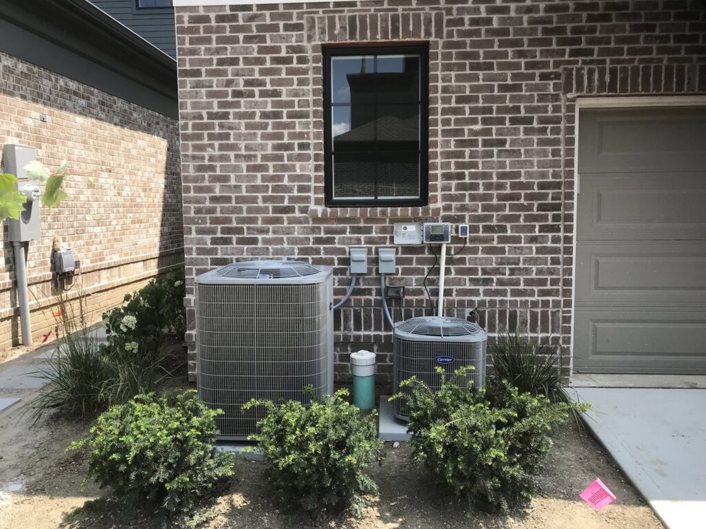 Two outdoor AC condenser units installed next to a brick residential building by Chad Byers - Edge Guys Heating & Cooling in Carmel, IN