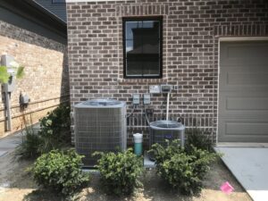 Two outdoor AC condenser units installed next to a brick residential building by Chad Byers - Edge Guys Heating & Cooling in Carmel, IN