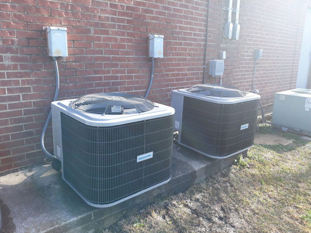 Two outdoor AC condenser units installed next to a brick wall by Go West A/C & Heating in Fort Worth, TX.