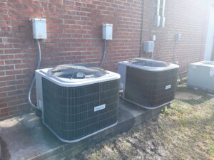 Two outdoor AC condenser units installed next to a brick wall by Go West A/C & Heating in Fort Worth, TX.