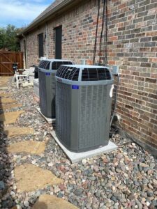 Two outdoor AC units installed next to a brick house by Fort Worth Air Conditioning Co. Inc. in Fort Worth, TX.