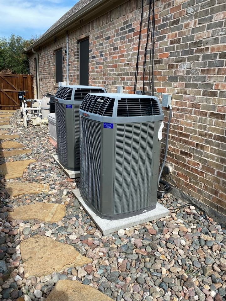Two outdoor AC units installed next to a brick house by Fort Worth Air Conditioning Co. Inc. in Fort Worth, TX.