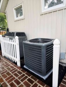 Two outdoor air conditioning units installed next to a residential building by Stoker Mechanical Heating & Air Conditioning in Lawrence, KS.
