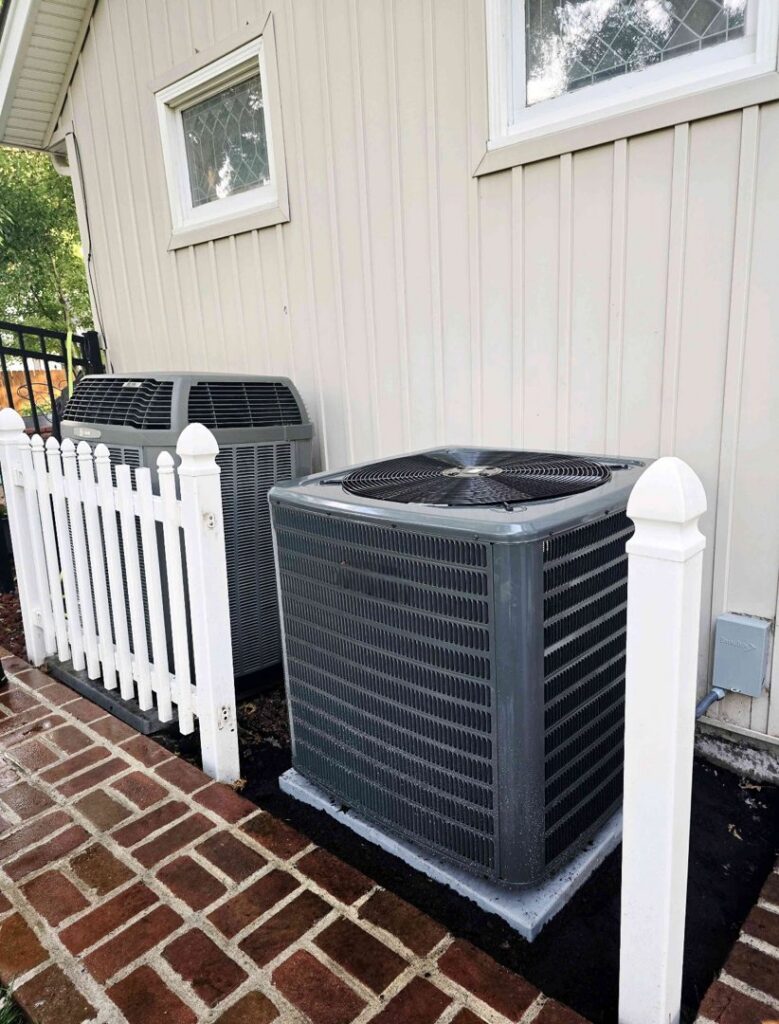 Two outdoor air conditioning units installed next to a residential building by Stoker Mechanical Heating & Air Conditioning in Lawrence, KS.