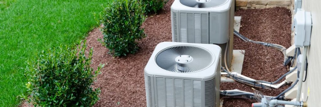 Two outdoor air conditioning units installed in a landscaped area by Reid Plumbing & Heating in Manhattan, KS.