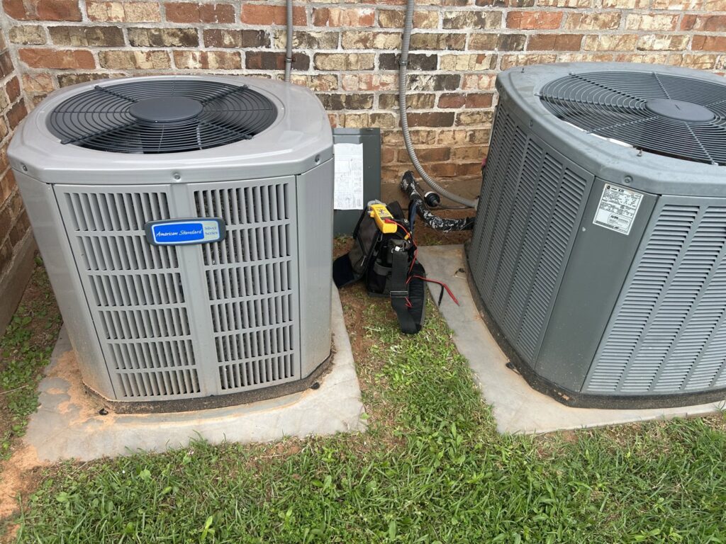 Two outdoor AC units, one American Standard, with a technician's tool bag during a service call by Air Advisors of Louisiana in Shreveport, LA.
