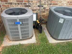 Two outdoor AC units, one American Standard, with a technician's tool bag during a service call by Air Advisors of Louisiana in Shreveport, LA.