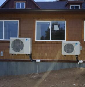 Two outdoor heat pump units professionally installed on the side of a brown house by The Heat Pump Store in Portland, OR.