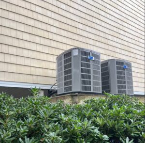 Two outdoor HVAC condenser units installed next to a house with cedar shake siding by Joe's Heating & Air Repair LLC in Surf City, NC