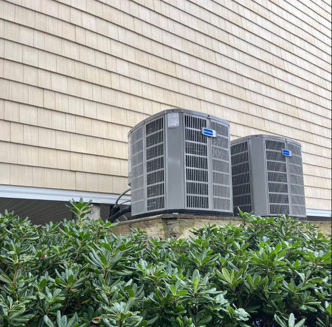 Two outdoor HVAC condenser units installed next to a house with cedar shake siding by Joe's Heating & Air Repair LLC in Surf City, NC