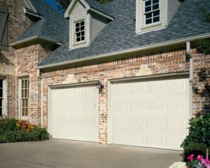 A brick house featuring two light-colored paneled garage doors by Overhead Door Company of Knoxville in Knoxville, TN
