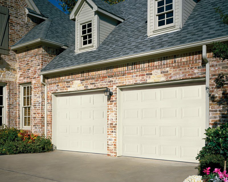 A brick house featuring two light-colored paneled garage doors by Overhead Door Company of Knoxville in Knoxville, TN