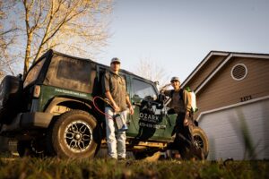 Two pest control technicians with their equipment and branded vehicle from Ozark Pest Control in Fayetteville, AR.