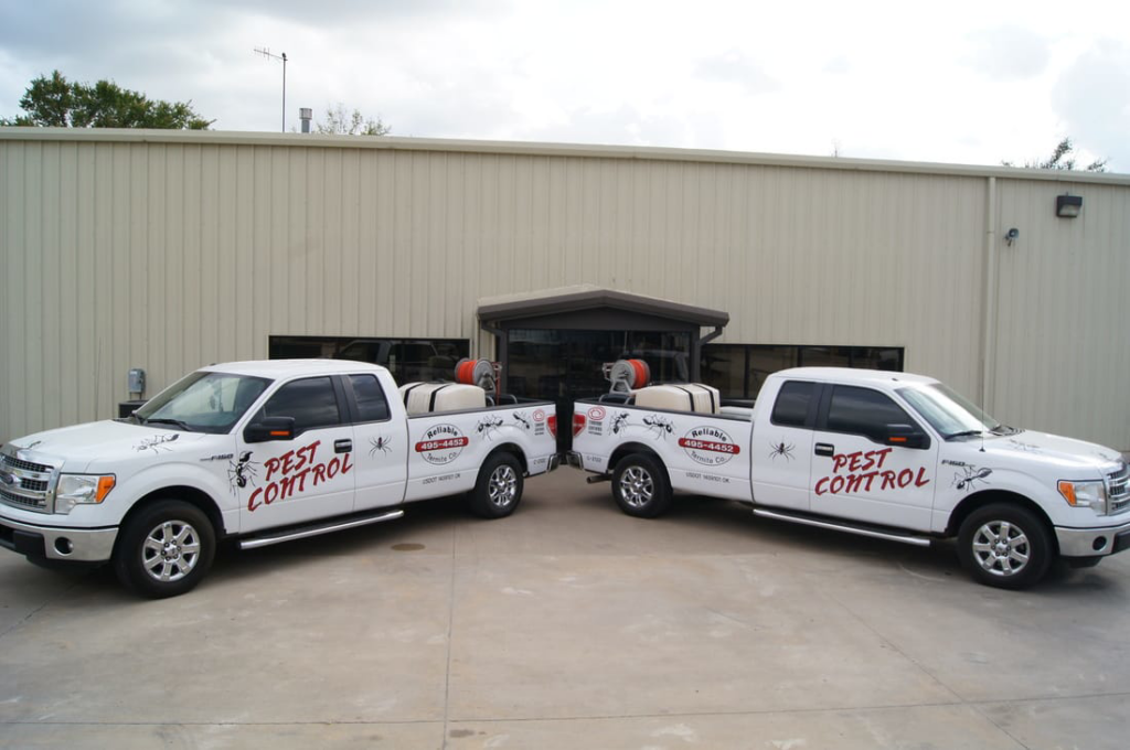 Two white pest control trucks from Reliable Termite of OKC parked outside a commercial building in Oklahoma City, OK.