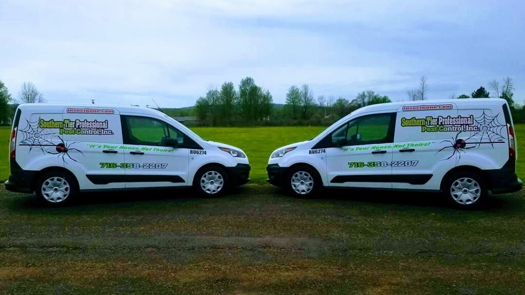 Two white pest control vans for Southern Tier Professional Pest Control Inc. in Randolph, NY, parked in a grassy area.