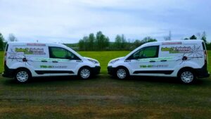 Two white pest control vans for Southern Tier Professional Pest Control Inc. in Randolph, NY, parked in a grassy area.
