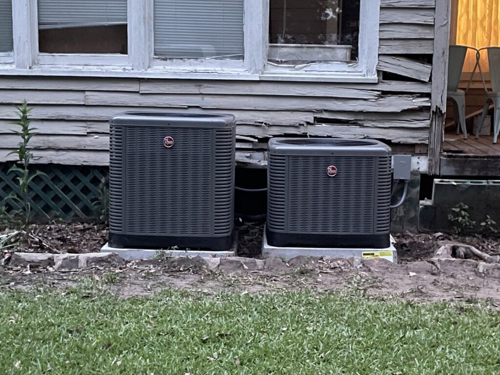 Two Rheem outdoor air conditioning units installed next to a residential building by Total Living Comfort in Irvington, AL.