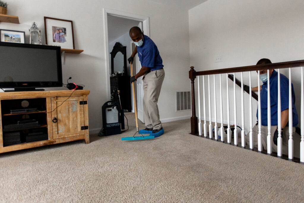 Two Hydro Clean technicians, wearing masks and shoe covers, professionally cleaning a carpeted area in a residential home in Baltimore, MD.