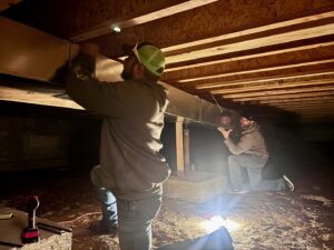 Two technicians from Lee's Heating & Cooling installing HVAC ductwork in a crawl space in Pueblo, CO.