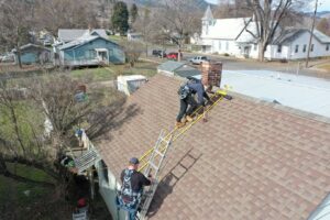 Two Chimney Wizards LLC technicians on a roof with ladders, performing chimney service near a brick chimney in Orofino, ID.