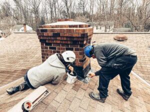 Two technicians performing repair work on a chimney on a roof for Rooftop Chimney Sweeps in Alexandria, VA.
