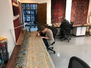 Two technicians diligently repairing rugs in the workshop of Renaissance Rug Cleaning Inc. in Portland, OR.