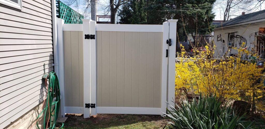 A newly installed two-tone vinyl fence gate next to a house with yellow flowers by Brothers Fence in Elizabeth, NJ.