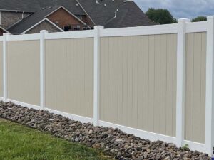 A modern two-tone vinyl privacy fence with decorative rocks installed by Frontier Fence LLC Bowling Green,Ky