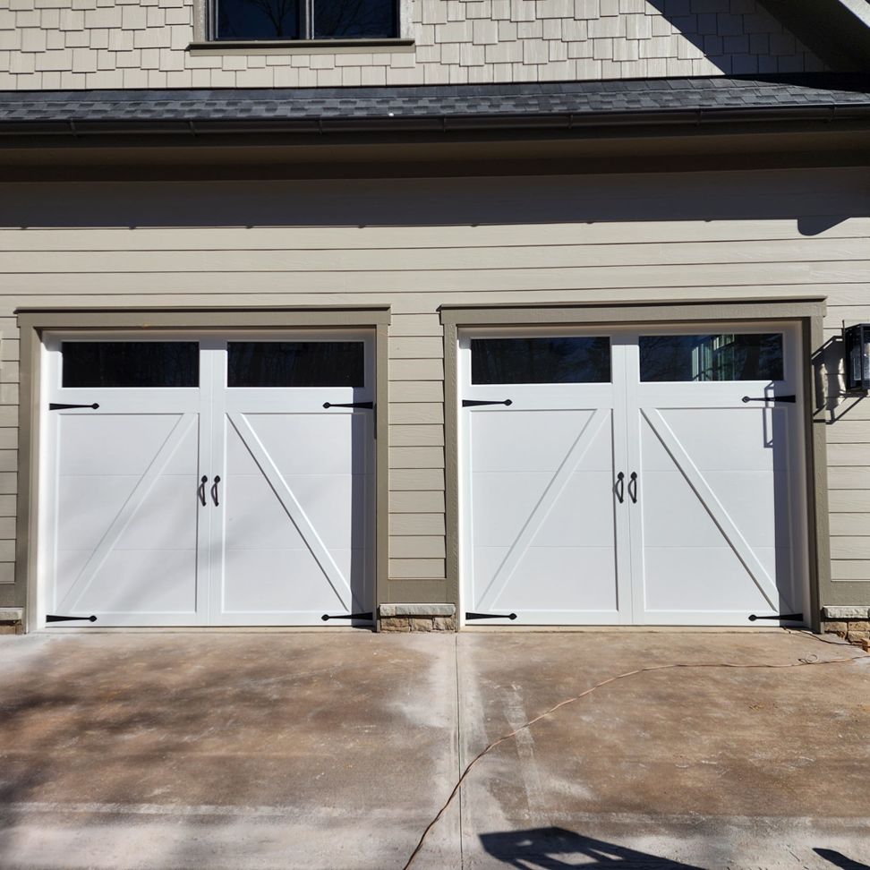 Two white carriage-style garage doors with decorative hardware installed by Getsinger's Overhead Doors in Spartanburg, SC.