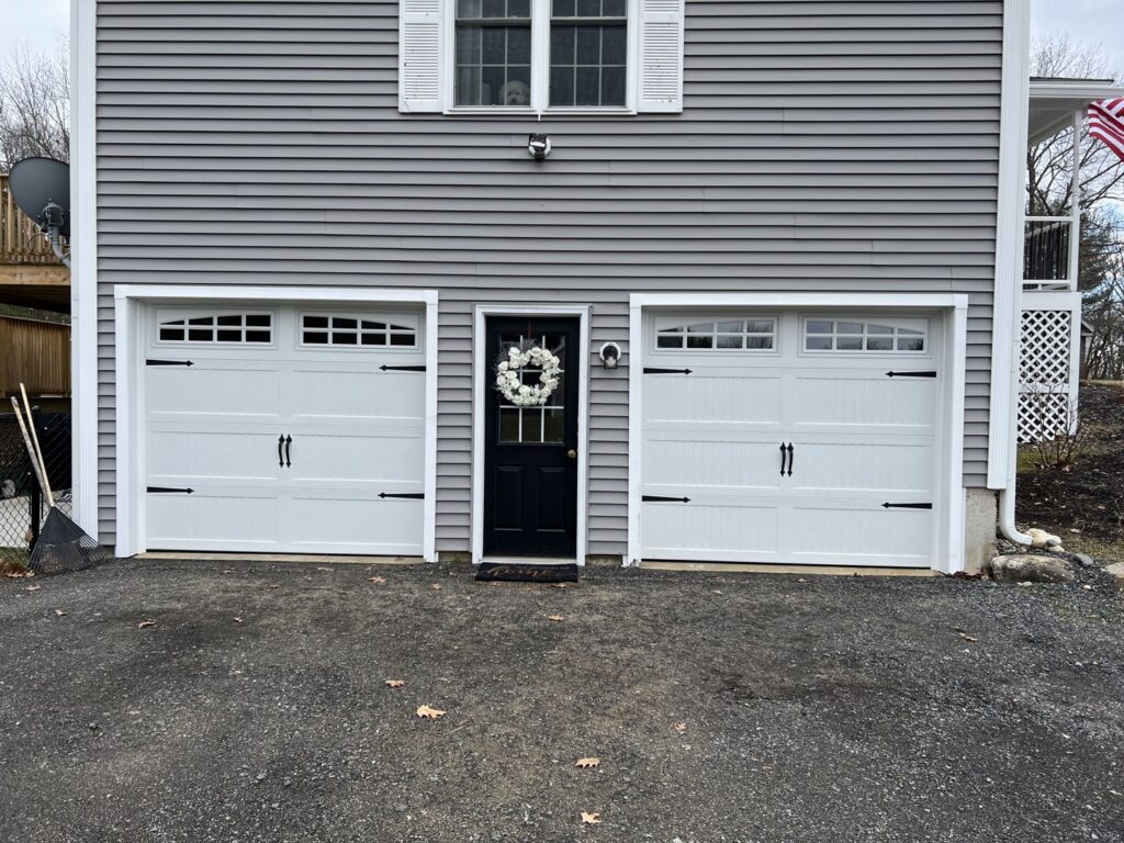 Two white garage doors with decorative hardware and windows installed by PM Garage Door in Hudson, NH.