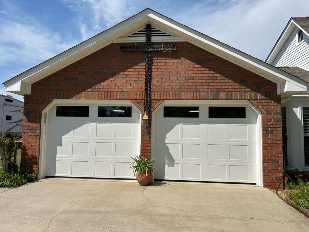 Two white garage doors with top windows installed on a brick house by Signature Garage Doors in Huntsville, AL.