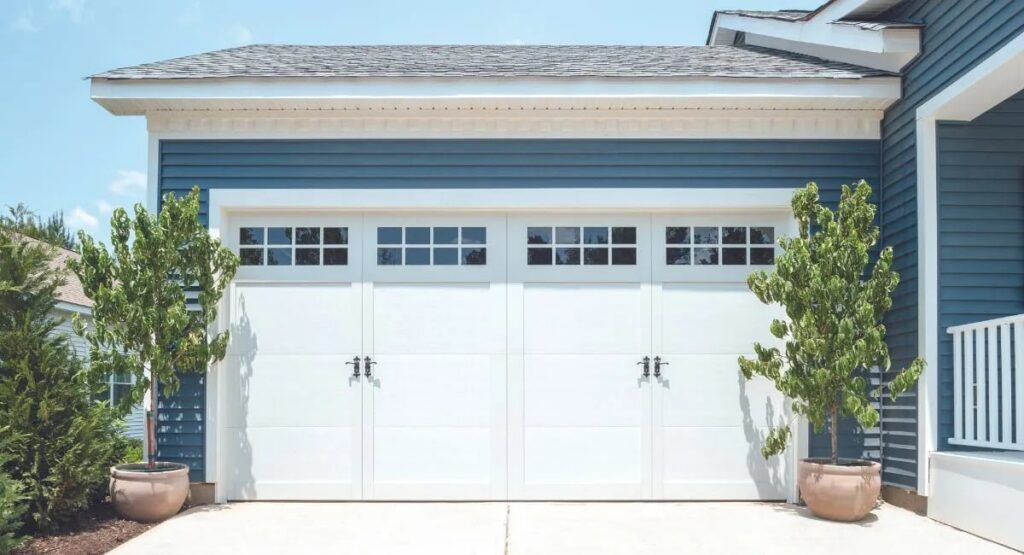 Two white garage doors with top windows installed on a blue residential house by Overhead Doors Unlimited, LLC in Appleton, WI.