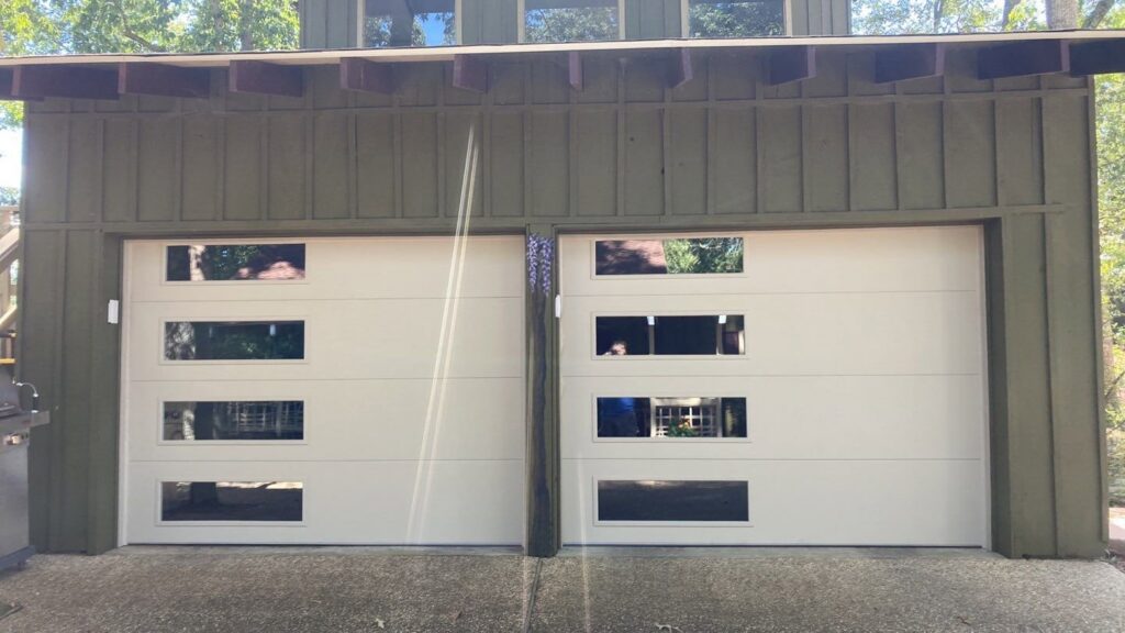 Two white garage doors with rectangular windows installed on a green house by Signature Garage Doors in Huntsville, AL.