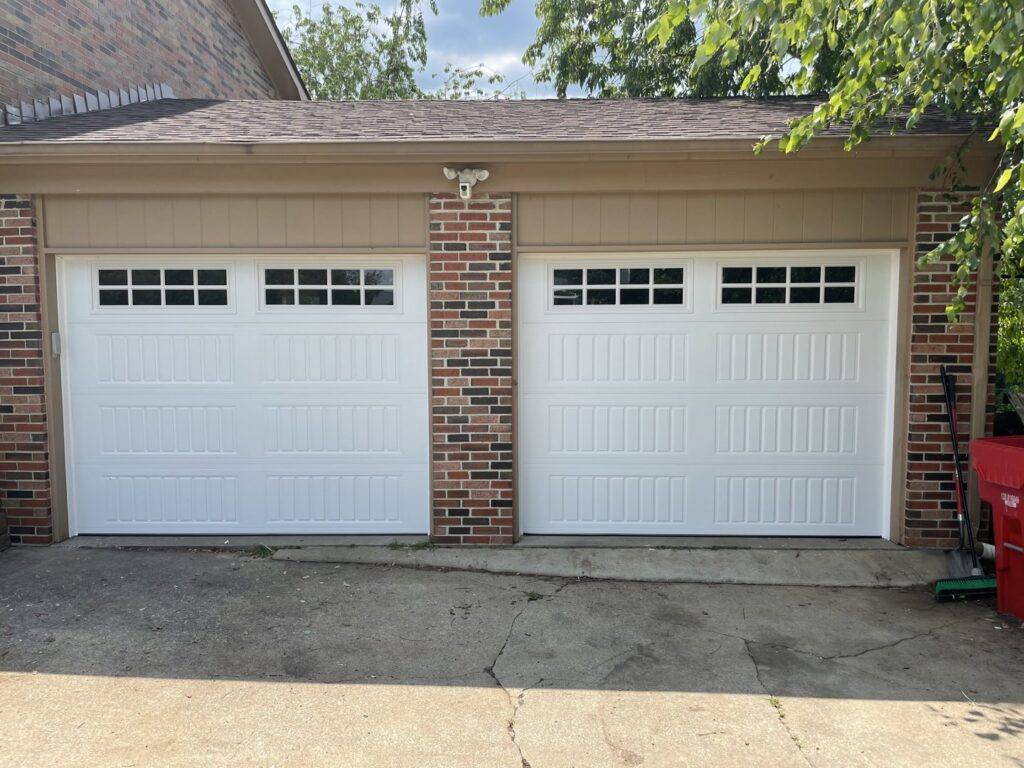 Two newly installed white panel garage doors with windows on a brick residential home by PRO-Line Garage Doors LLC in Richmond, KY.