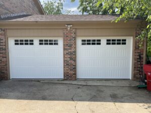 Two newly installed white panel garage doors with windows on a brick residential home by PRO-Line Garage Doors LLC in Richmond, KY.