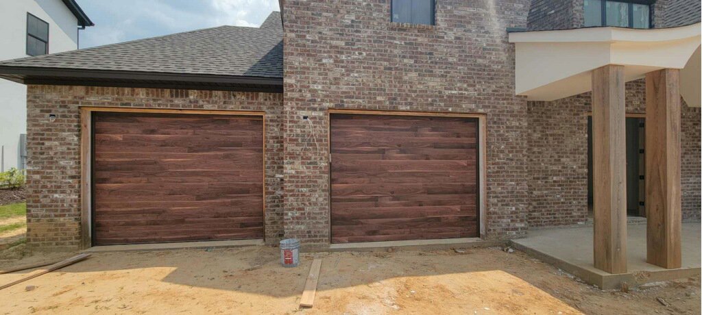 Two new wood-grain garage doors installed on a modern brick house by Geaux Overhead Door in West Monroe, LA.