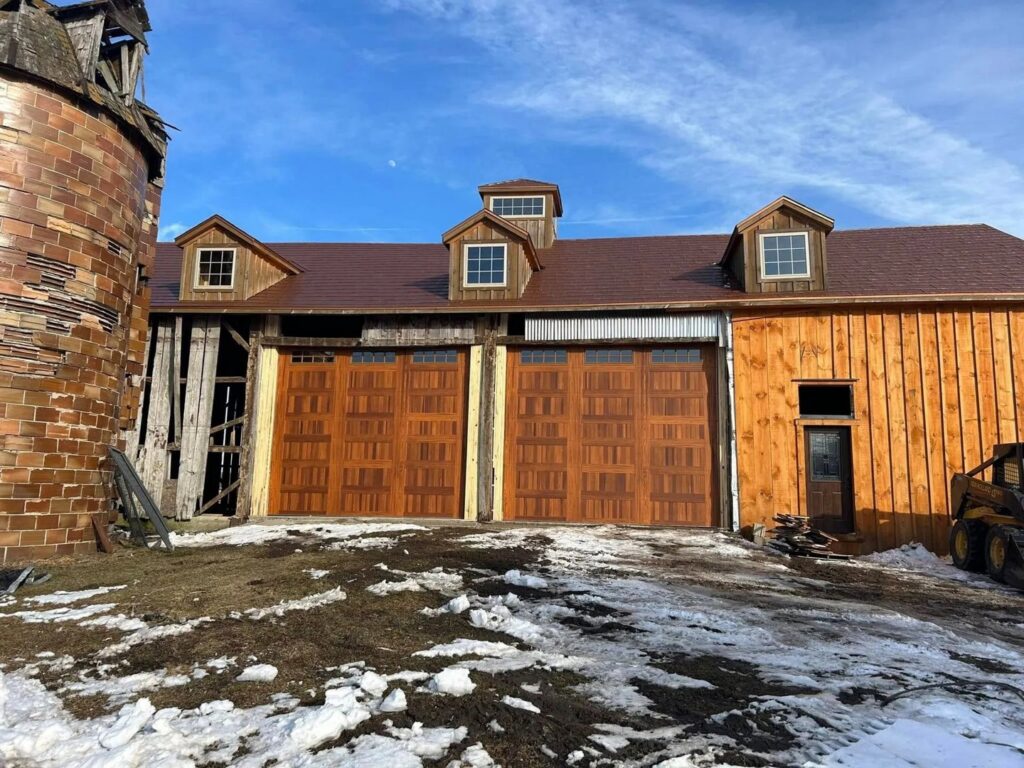 Two wood-look garage doors with top windows installed on a barn-style building by Overhead Doors Unlimited, LLC in Appleton, WI.