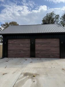 Two new wood-look garage doors installed on a black modern building by Geaux Overhead Door in West Monroe, LA.