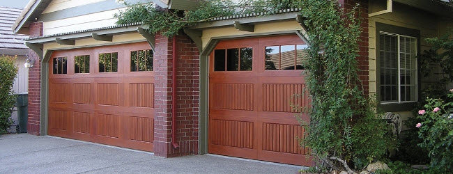 Two attractive wood-style garage doors with top windows on a brick home by Overhead Door Company of Evansville in Evansville, IN.