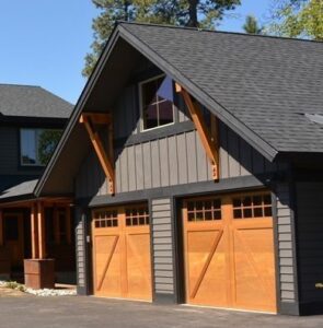 Two wooden-style garage doors with windows on a dark-sided residential home by SCI Door in Yakima, WA