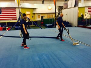 Two workers cleaning a large blue carpeted area with professional equipment for Spectrum Cleaning & Restoration in Medford, OR