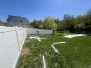 Two workers installing white vinyl fence panels in a residential yard for Fence Pros LLC in Medford, OR.